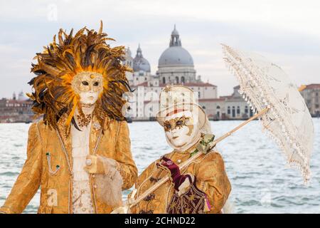 Venedig, Venetien, italien - Paar in Kostüm beim Karneval in Venedig vor der Kulisse der Basilika Santa Maria della Salute und Lagune Stockfoto