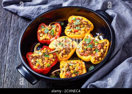 Gefüllte Paprika mit Hackfleisch, Mais und Käse in einer schwarzen Backform auf einem Holztisch, horizontale Ansicht von oben, Nahaufnahme Stockfoto