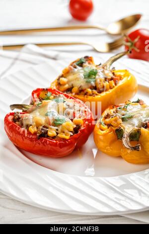 Klassische gefüllte Paprika mit Hackfleisch, Mais und Käse auf einem weißen Teller auf einem Holztisch mit goldenem Besteck, vertikale Ansicht, Nahaufnahme Stockfoto