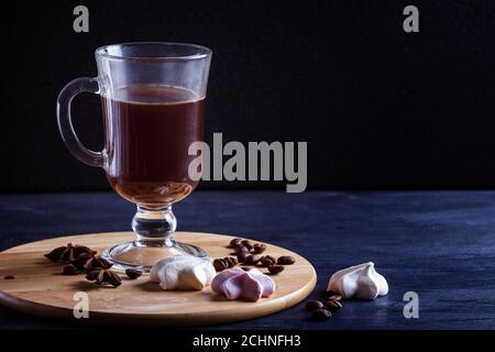 Glas Tasse Kaffee mit Baseen auf einem Holzbrett auf schwarzem Hintergrund. Nahaufnahme, Kopierraum. Stockfoto