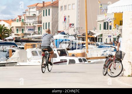 Vodice, Kroatien - 1. September 2020: Mann im Matrosen T-Shirt auf dem Fahrrad auf der Hafenpromenade in der mediterranen Stadt am Meer Stockfoto