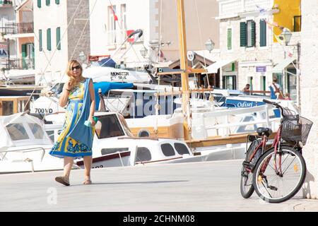 Vodice, Kroatien - 1. September 2020: Junge Frau auf dem Dock mit Booten und einem geparkten Fahrrad zu Fuß Stockfoto