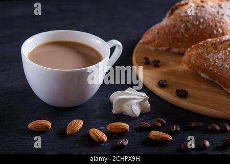 Weiße Tasse Kaffee mit Sahne und Brötchen auf schwarzem Hintergrund. Nahaufnahme. Stockfoto