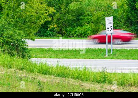 Horizontaler Schuss eines schnellen roten Autos Streifen durch ein Tempolimit-Zeichen. Unschärfe zeigt Bewegung. Stockfoto