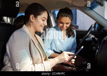Seitenansicht Porträt von zwei jungen Frauen aus dem Nahen Osten mit dem Smartphone Und lächelnd im Auto sitzen Stockfoto