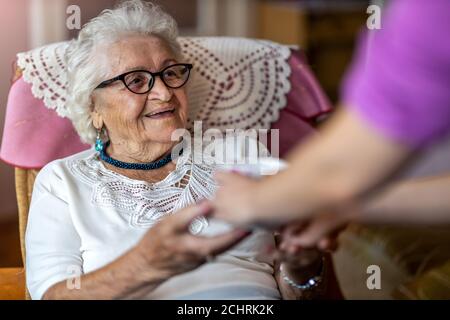 Hilfreiche häusliche Krankenschwester gibt einer älteren Frau eine Tasse Von heißem Tee Stockfoto