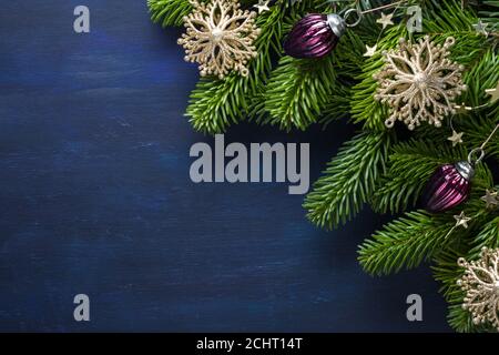 Tannenzweig mit weihnachtlicher Dekoration auf einem dunkelblau bemalten Holzhintergrund. Flach liegend. Weihnachten Hintergrund mit Platz für Text. Stockfoto