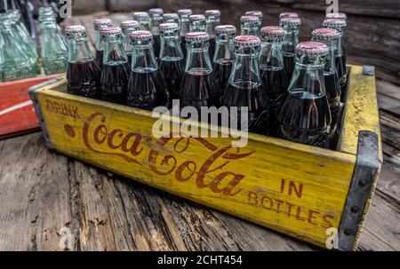 Alte Coca-Cola Glasflaschen mit Cola noch in den Flaschen In einer hölzernen Lieferkiste auf einem Holzboden sitzend Nahaufnahme Stockfoto