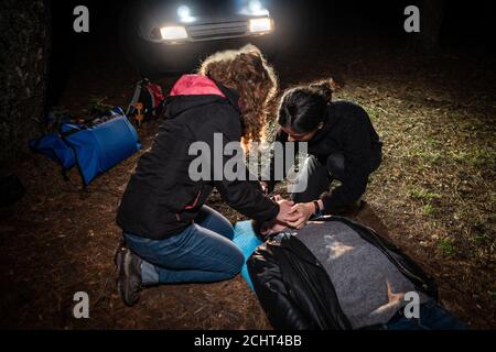 Erste-Hilfe-Training Vor Ort. Zwei Frauen helfen einem Mann an den Scheinwerfern eines Autos. Stockfoto