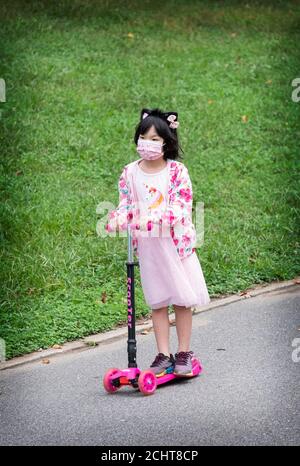 Ein extrem süßes asiatisch-amerikanisches Mädchen, das in Rosa gekleidet ist, fährt ihren Allrad-Roller in einem Park in Queens, New York City. Stockfoto