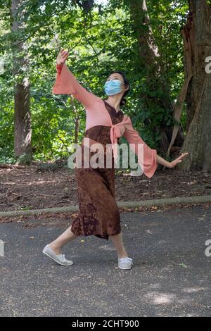 Umgeben von Bäumen und Laub tanzt eine anmutige chinesisch-amerikanische Tänzerin zu traditioneller Volksmusik. Ich habe einen Park in Queens, New York City Stockfoto