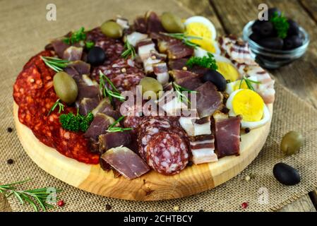 Holzschneidebrett mit Schinken, Speck, Würstchen, gekochten Eiern und Oliven auf altem Tisch. Selektiver Fokus. Stockfoto