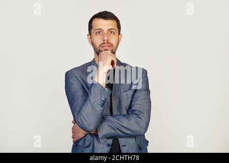 Porträt eines jungen männlichen Unternehmers, der mit traurigem Gesicht auf die Kamera schaut, eines Geschäftsmannes, enttäuscht von Verlusten im Geschäft. Der Mann schaut auf die Kamera, isoliert durch eine graue Wand mit. Stockfoto