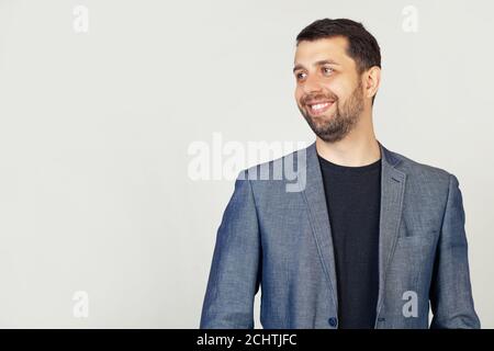Nahaufnahme eines hübschen bärtigen Typen in einer Jacke, die im Profil steht, zur Seite schauend, für ein Foto posierend. Ein Mann, der mit einem Lächeln auf dem Gesicht zur Seite blickt, natürlicher Ausdruck. Stockfoto