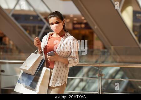 Waist up Porträt der jungen Frau trägt Maske beim Einkaufen in Mall und Blick auf Kamera, kopieren Raum Stockfoto