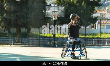 Junger, hübscher Mann im Rollstuhl, der Basketball spielt Stockfoto