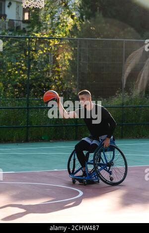 Junger, hübscher Mann am Rollstuhl, der Basketball spielt Stockfoto