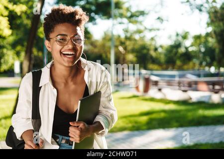 Bild der optimistischen afrikanischen Frau zu Fuß im Park, während Laptop in der Hand Stockfoto