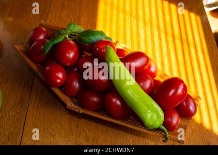 Kleine rote Tomaten und grüne Paprika im Korb auf einem Holztisch , selektive Fokus Stockfoto