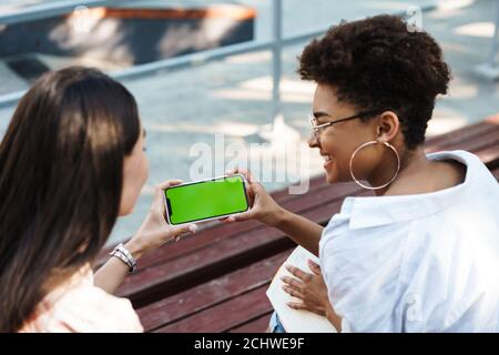 Draufsicht auf zwei glückliche junge Freunde, die sich einen leeren Bildschirm teilen Handy im Park Stockfoto