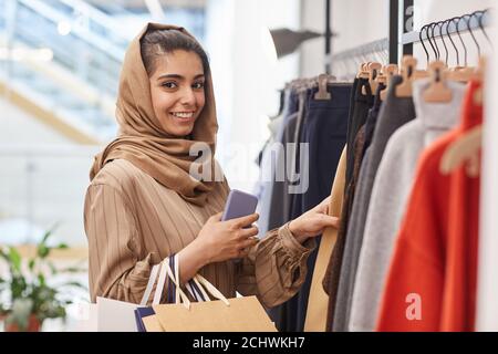 Waist up Porträt von eleganten jungen Frau Blick auf die Kamera Beim Stehen an Kleiderstangen und beim Einkaufen im Einkaufszentrum Stockfoto