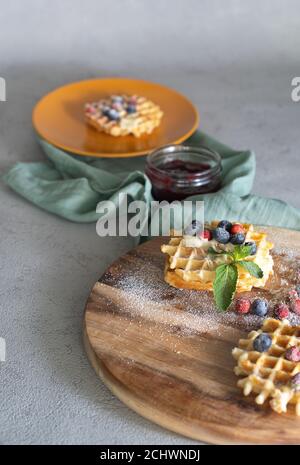 Rundes Holzhackbrett mit Waffeln gefüllt mit Erdbeermarmelade Und Heidelbeere mit Minze und Heidelbeere auf weichem Hintergrund Stockfoto