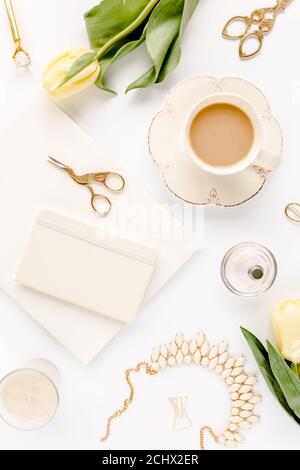 Weiblicher Arbeitsplatz mit gelben Tulpenblüten, Damenmode goldene Accessoires, Tagebuch, Gläser auf weißem Hintergrund. Flach liegend. Draufsicht Hintergrund. Stockfoto