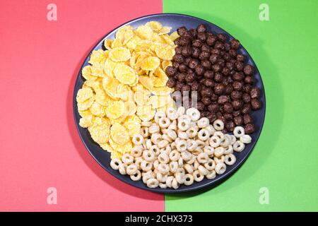 Honigringe, Cornflakes und Schokoladenkugeln auf schwarzem Teller auf farbigem Hintergrund. Gesunde Ernährung Konzept. Draufsicht. Stockfoto