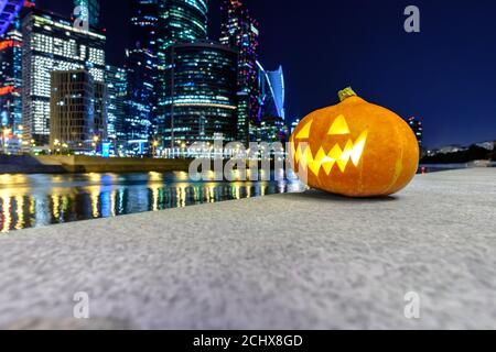 Halloween Kürbis auf dem Hintergrund der Moskauer Stadt Wolkenkratzer in der Nacht. Mehrstöckige Gebäude und verschwommene farbige Lichter der Stadt spiegeln sich in der wider Stockfoto