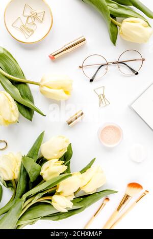 Weiblicher Arbeitsplatz mit gelben Tulpenblüten, Damenmode goldene Accessoires, Tagebuch, Gläser auf weißem Hintergrund. Flach liegend. Draufsicht Hintergrund. Stockfoto