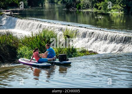Zwei Paddelboarder machen eine Pause in Warleigh Weir am Fluss Avon in Somerset, da die Septembertemperaturen hoch bleiben. Stockfoto