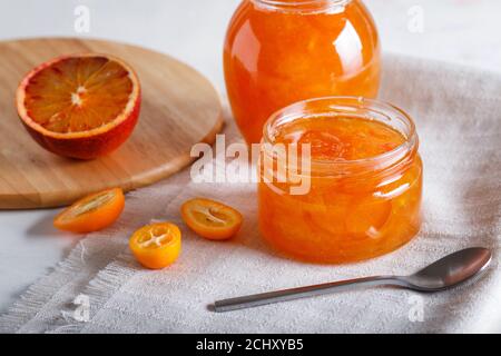Orangen- und Kumquatmarmelade in einem Glas mit frischen Früchten auf einer weißen Leinentischdecke. Hausgemacht, Nahaufnahme. Stockfoto