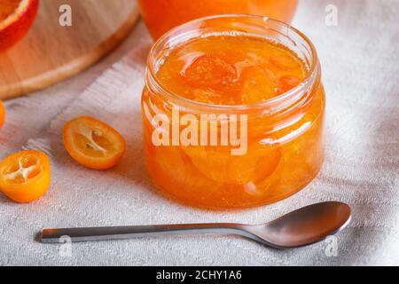 Orangen- und Kumquatmarmelade in einem Glas mit frischen Früchten auf einer weißen Leinentischdecke. Hausgemacht, Nahaufnahme. Stockfoto