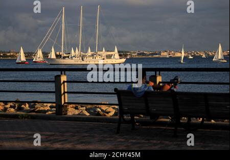 Mann, der sich auf einer Bank am Hudson River Waterfront Walkway entspannt Mit Segelbooten im Wasser der Upper New York Bay Im Hintergrund.Liberty State Park NJ.USA Stockfoto