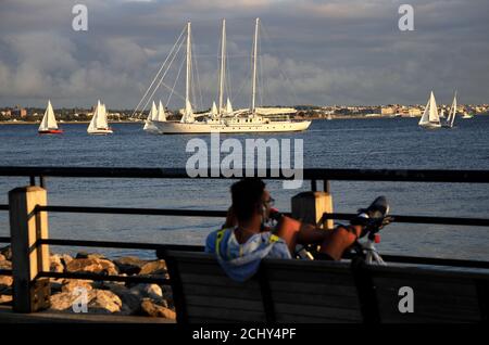 Mann, der sich auf einer Bank am Hudson River Waterfront Walkway entspannt Mit Segelbooten im Wasser der Upper New York Bay Im Hintergrund.Liberty State Park NJ.USA Stockfoto