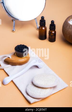 Home Self-Care-Kit für Gesichtsmassage. Trockene Lymphdrainage Pinsel, Derma mezoroller, Loofah Pads, natürliches Öl Serum auf Leinenbeutel auf beigem Hintergrund. Stockfoto