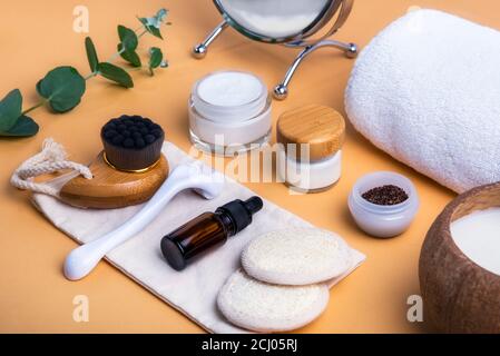 Home Self-Care-Kit für Gesicht. Trockene Lymphdrainage Massage Bürste, mezoroller, Loofah Pads, Naturserum, Scrab, Creme, Handtuch auf beigem Hintergrund. DI Stockfoto