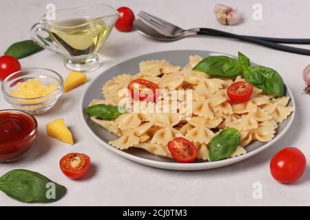 Farfalle Pasta mit Kirschtomaten, Tomatensauce und Basilikum auf weißem Hintergrund, Nahaufnahme Stockfoto