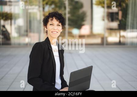 Porträt von lächelnden kaukasischen Geschäftsfrau in Anzug sitzen mit Laptop Außerhalb des Büros Stockfoto