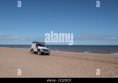 Graue Strandpatrouille Land Rover 90 Station wagen wird entlang des Sandstrandes von Anderby, an der Linclonshire Küste Linie, England gefahren. Stockfoto