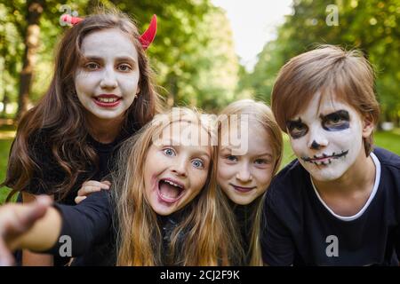 Gruppe von fröhlichen Kindern in Halloween-Kostümen und Gesichtsbemalung Blick auf die Kamera während der Aufnahme Selfie-Foto im Freien Stockfoto