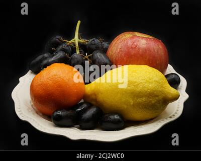 Apfel, Zitrone, Orange und Trauben auf weißem Teller Stockfoto