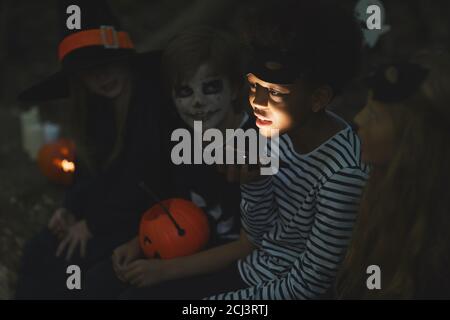 Multiethnische Gruppe von Kindern, die gruselige Geschichten an Halloween erzählen, konzentrieren sich auf afroamerikanischen Jungen, der Taschenlampe im Vordergrund hält Stockfoto