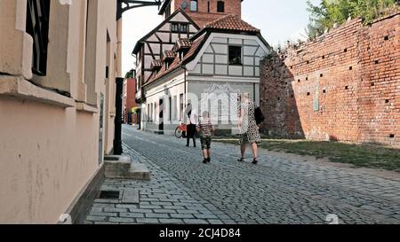 Drei Personen gehen auf einer gepflasterten Straße in der Altstadt von Torun, Polen. Stockfoto