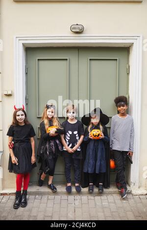 Vertikale voller Länge Porträt der multi-ethnischen Gruppe von Kindern tragen Halloween Kostüme Blick auf Kamera während Trick oder behandeln zusammen Stockfoto