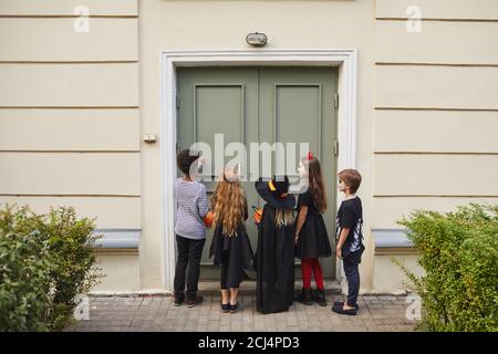 Rückansicht bei multi-ethnischen Gruppe von Kindern tragen Halloween-Kostüme Klingeln Türklingel während Trick oder Behandlung zusammen, kopieren Raum Stockfoto