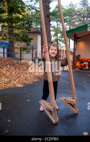 Kleines Mädchen versucht Stelzen auf einem Bürgersteig. Halloween-Display im Hintergrund. Stockfoto