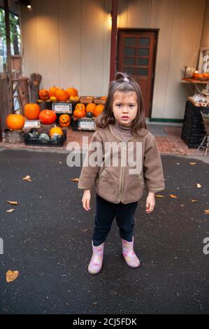 Kleines Mädchen in brauner Fleecejacke wartet auf Halloween vor einem Haus mit Kürbissen Display. Stockfoto