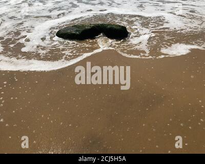 Meeresströmung, Sand, Schaum und Felsen. Stockfoto