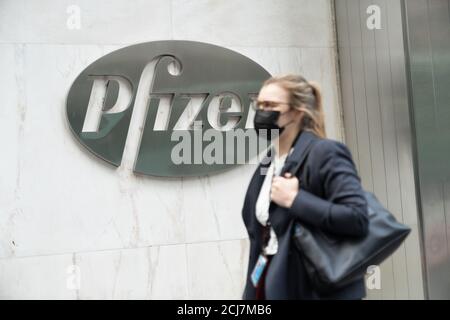 New York, Usa. September 2020. Eine Frau, die eine Gesichtsmaske trägt, geht an einem Pfizer-Logo in ihrem Hauptsitz vorbei.Pfizer Corona-Virus-Impfstoff könnte vor Ende des Jahres an Amerikaner abgegeben werden, sagt CEO. Kredit: SOPA Images Limited/Alamy Live Nachrichten Stockfoto